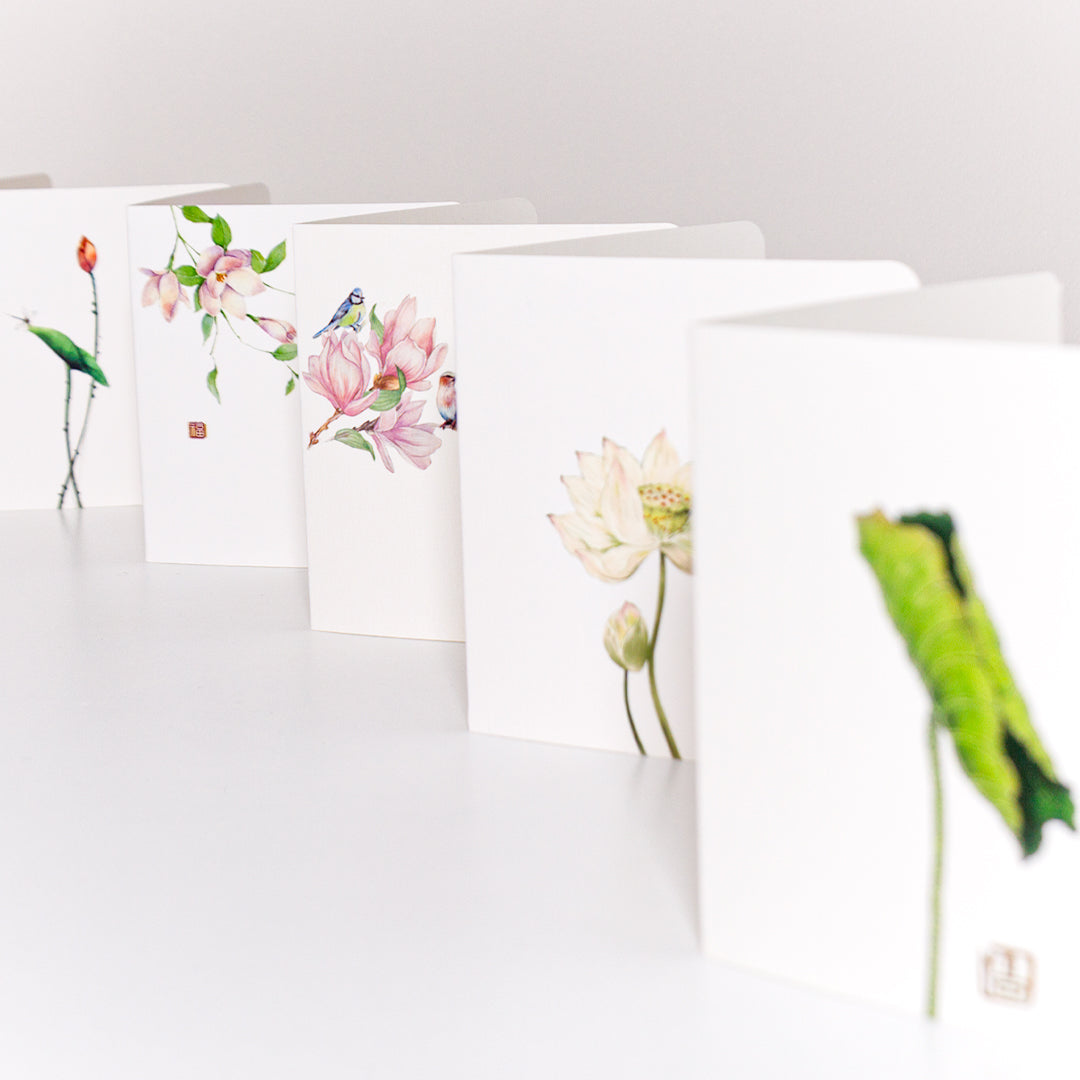 A display of the Eastern Essence Collection greeting cards, featuring all designs: Blooming Lotus Letter, Leaf of Tranquility Letter, Melodies That Linger Letter, Songs of Spring Letter, and Twin Lotus Blossoms Letter. Each card showcases delicate watercolor artwork inspired by nature, arranged elegantly in a cascading formation.